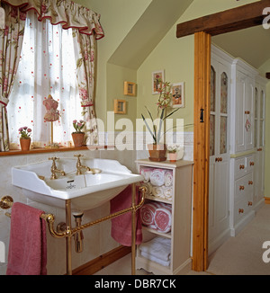 Voile blanc et des rideaux sur la fenêtre au-dessus du bassin dans une salle de bains privative avec des serviettes roulées stockés sur étagère Banque D'Images