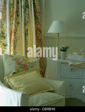 Chambre avec yellow vérifié et coussins à motifs de roses sur le fauteuil en face de la fenêtre avec des rideaux à motifs de roses Banque D'Images