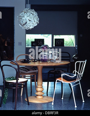 Chaises en bois cintré et blanc chaise en métal et bois circulaire à table dans la salle à manger moderne avec abat-jour en plastique blanc Banque D'Images