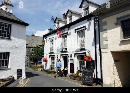 Un homme avec deux chiens en laissant le Red Lion Inn de Hawkshead, une petite ville pittoresque dans le Lake District, dans le Nord de l'Angleterre. Banque D'Images