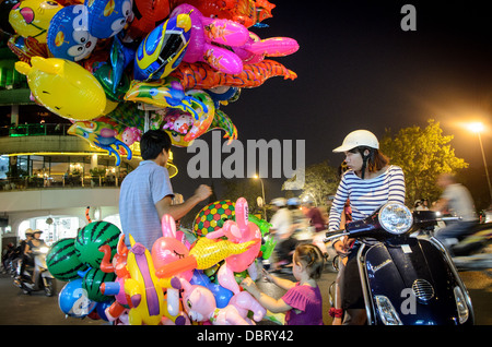 HANOI, Vietnam — Une jeune fille vietnamienne admire les ballons d'hélium à vendre dans une rue du vieux quartier de Hanoi, tandis que sa mère regarde. Banque D'Images