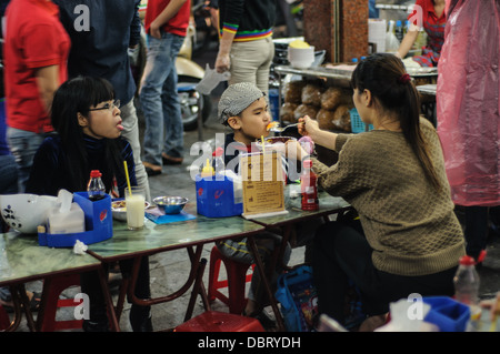 HANOI, Vietnam — Une mère nourrit son jeune fils chez un vendeur de nourriture de rue dans le vieux quartier de Hanoi. Banque D'Images