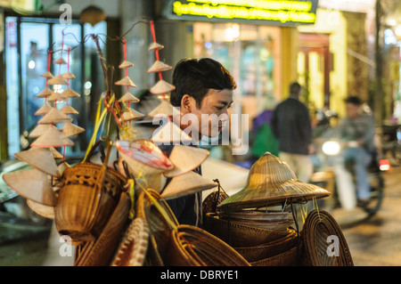 HANOI, Vietnam — Un vendeur de rue vend des chapeaux coniques vietnamiens et des souvenirs connexes dans une rue du vieux quartier de Hanoi. Banque D'Images