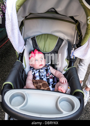 Adorable baby girl animé se trouve dans l'élégant quartier de poussette portant des cheveux rouge à pois bleu barboteuse band & vérifié sur une rue de New York Banque D'Images