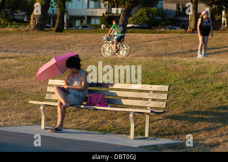 Femme lisant à l'ombre d'un parapluie le long de Sunset Beach Park - West End, Vancouver, British Columbia, Canada Banque D'Images