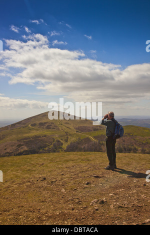 Un marcheur avec des jumelles sur le sommet de la colline nord dans les collines de Malvern, Worcestershire, Angleterre, RU Banque D'Images