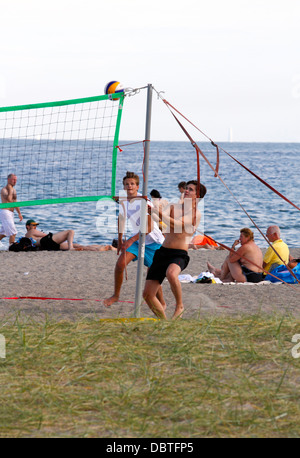 Adolescents garçons sur la plage jouant au Beach volley pour le plaisir de l'amusement sur un après-midi chaud et ensoleillé d'été à la côte de Øresund. Hygge danois. Banque D'Images