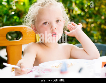 Little girl eating et surpris. La jeune fille a un drôle d'expression et elle est en train de manger en plein air Banque D'Images