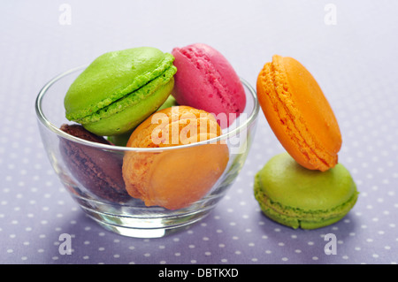 Macarons colorés dans bol en verre sur fond violet Banque D'Images