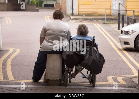 Deux dames s'asseoir patiemment, sur double lignes jaunes, en attente d'un ascenseur. Banque D'Images