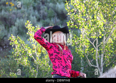 Jolie cowgirl à cheval dans le Montana ranch contre les arbres en contre-jour Banque D'Images