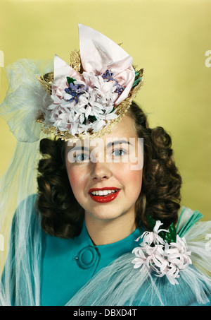 Années 1940 Années 1950 YOUNG SMILING WOMAN WEARING STRAW HAT AVEC FLEURS ET FILETS, LOOKING AT CAMERA Banque D'Images