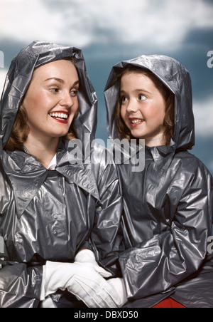 Années 1940 Années 1950 PORTRAIT SMILING Mother and Daughter WEARING Manteaux de pluie correspondant Holding Hands Banque D'Images