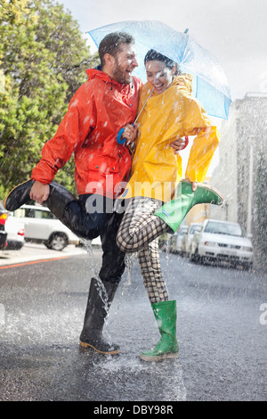 Couple heureux dans la région de Wellington splashing in rainy street Banque D'Images