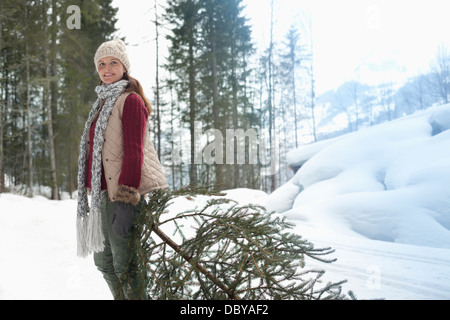 Portrait of smiling woman en faisant glisser l'arbre de Noël dans la neige fraîche Banque D'Images