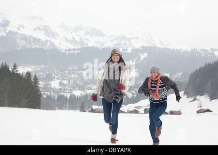 Heureux couple running in snowy field Banque D'Images