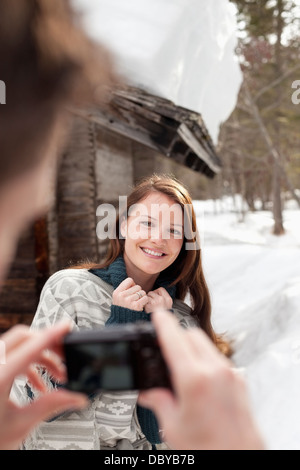 Man photographing smiling woman dans la neige à l'extérieur de cabine Banque D'Images