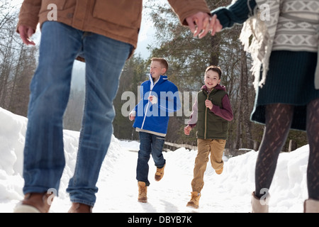 Enfants courant derrière les parents tenant les mains dans la neige Banque D'Images