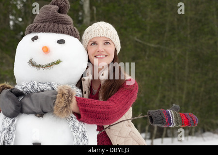 Happy woman hugging snowman in woods Banque D'Images