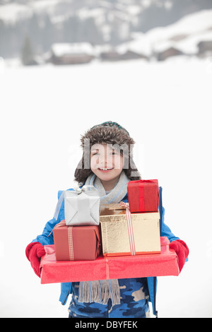 Portrait of smiling boy carrying pile de cadeaux de Noël dans la neige Banque D'Images