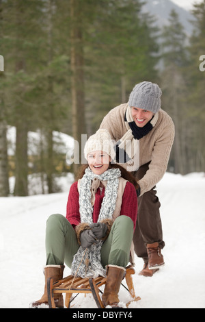 Heureux couple Sledding in Snowy Woods Banque D'Images