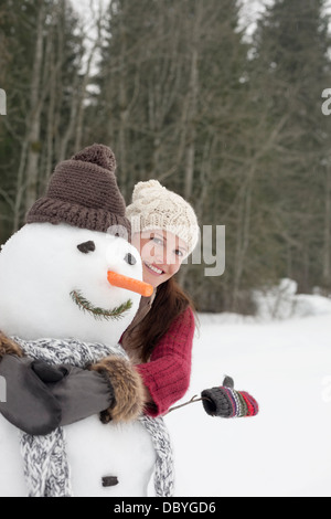 Happy woman hugging snowman in woods Banque D'Images