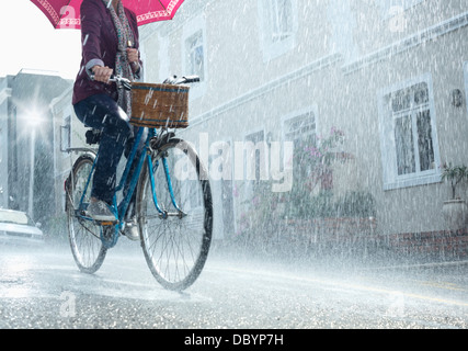 Woman riding bicycle with umbrella in rainy street Banque D'Images