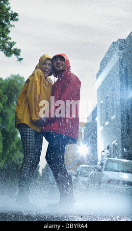 Couple heureux en tenant les mains d'imperméables dans la pluie Banque D'Images