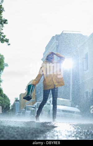 Femme en imperméable transportant Wellington et marche pieds nus dans la pluie Banque D'Images