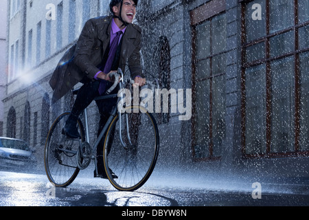 Homme d'enthousiaste riding bicycle in rainy street Banque D'Images