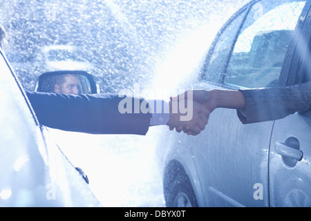 Businessman and businesswoman shaking des voitures dans la pluie Banque D'Images