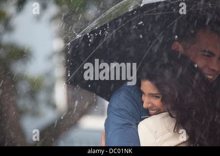 Heureux couple hugging under umbrella in rain Banque D'Images