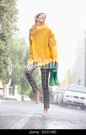 Happy woman dancing barefoot in rainy street Banque D'Images