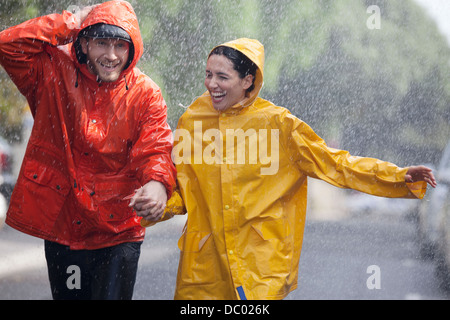 Heureux couple holding hands and running in rainy street Banque D'Images