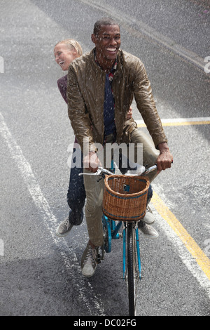 Heureux couple riding bicycle in rainy street Banque D'Images