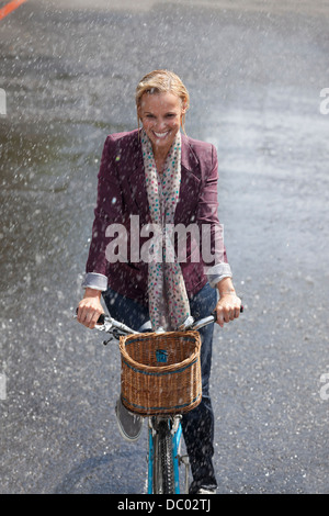 Happy woman riding bicycle in rainy street Banque D'Images