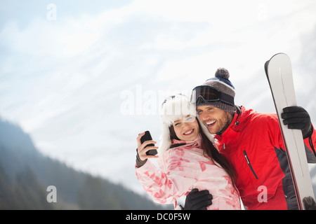 Couple heureux avec skis taking self-portrait with camera phone Banque D'Images