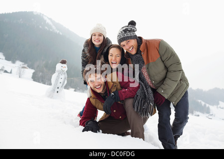 Portrait of happy friends in snowy field with snowman Banque D'Images