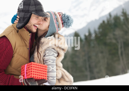 Heureux couple with Christmas Gift kissing in snowy field Banque D'Images