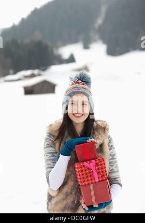 Portrait of smiling woman holding Christmas gifts in snowy field Banque D'Images