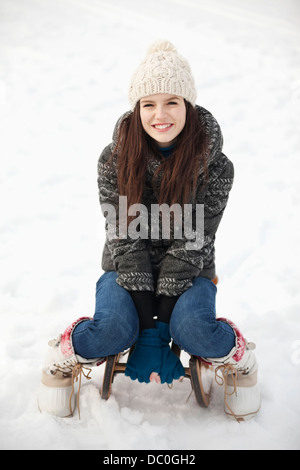 Portrait of smiling woman sitting on sled in snow Banque D'Images