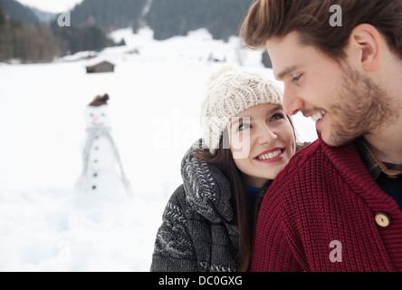 Close up of happy couple in snowy field with snowman Banque D'Images