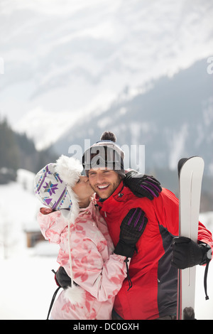 Couple heureux avec skis kissing in snowy field Banque D'Images