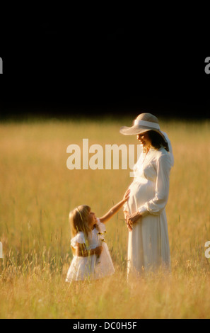 Années 1980 Années 1990, petite fille de toucher les mères enceintes debout estomac IN GRASSY FIELD Banque D'Images