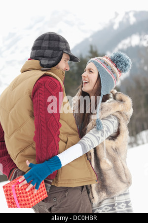 Une femme ayant atteint pour cadeau de Noël derrière le dos de l'homme in snowy field Banque D'Images