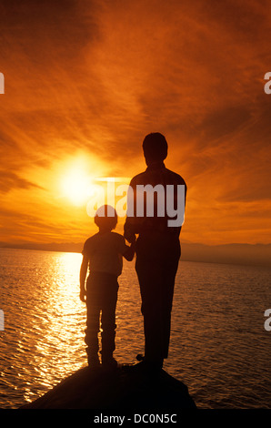 Des années 1990, la silhouette du père et fils regardant le coucher du soleil au-dessus de l'eau Banque D'Images