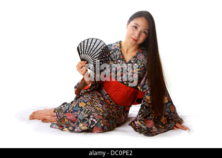 Japonais assis sur le plancher traditionnel portant un kimono à motifs bleu et rouge et la tenue d'un ventilateur Banque D'Images