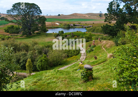 Hobbiton très vert avec chemin serpentant à travers l'image avec le lac et arbres en arrière-plan du Parti, montrant le trou de hobbit chimneys Banque D'Images