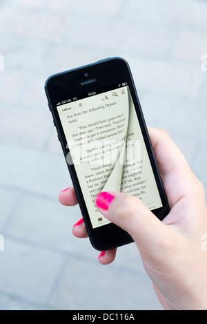 Femme tournant la page virtuelle d'un ebook avec l'app Apple iBooks sur iPhone 5 Banque D'Images