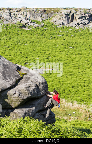 Un homme dans un t-shirt rouge et d'escalade bouldering à Burbage Valley dans le Peak District National Park, près de Sheffield, en Angleterre, Royaume-Uni Banque D'Images